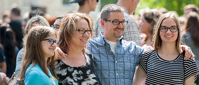 A group of four people, possibly a family, smiling and posing for a photo together in an outdoor setting crowded with people.